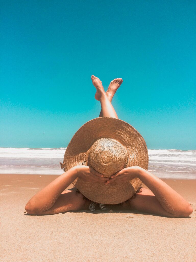 pexels-photo-1770310-1770310 A woman in a straw hat relaxes on a sunny beach, enjoying the clear blue sky and ocean waves.