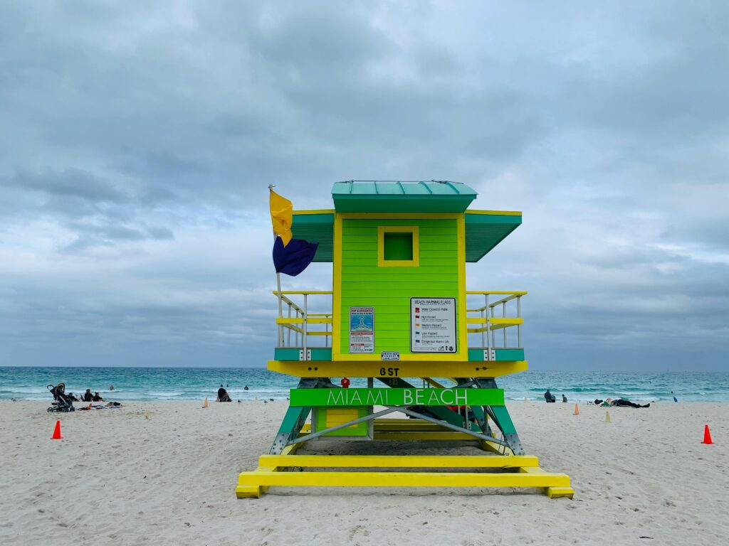 pexels-photo-4445179-4445179 Colorful lifeguard tower with clear beach in Miami Beach, Florida, under cloudy skies.